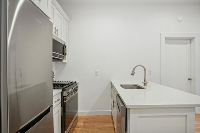 kitchen featuring light stone countertops, white cabinets, stainless steel appliances, sink, and light wood-type flooring