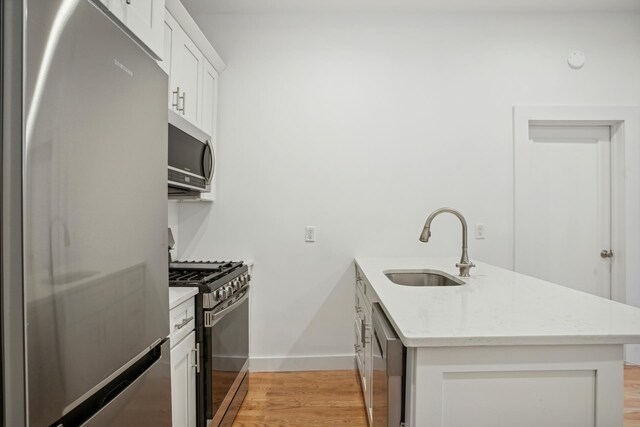 kitchen with sink, white cabinets, stainless steel appliances, light stone countertops, and light hardwood / wood-style flooring