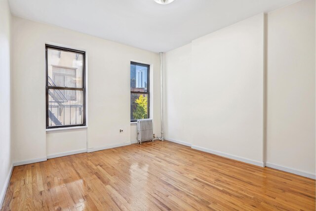 spare room with radiator heating unit and light hardwood / wood-style flooring