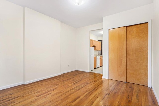 unfurnished bedroom featuring light wood-type flooring, a closet, and white refrigerator