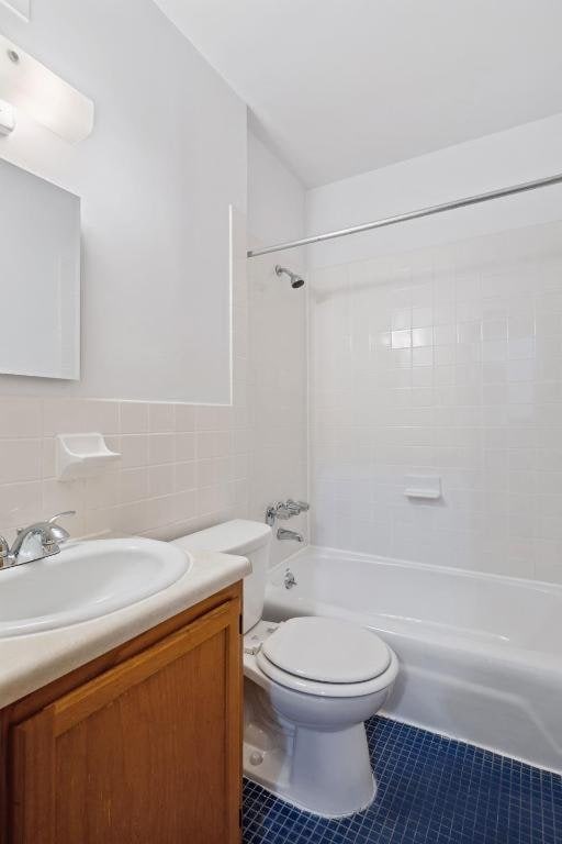 full bathroom featuring toilet, vanity, tile walls, tile patterned flooring, and tiled shower / bath combo