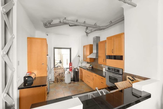 kitchen featuring a sink, dark countertops, appliances with stainless steel finishes, and wall chimney exhaust hood