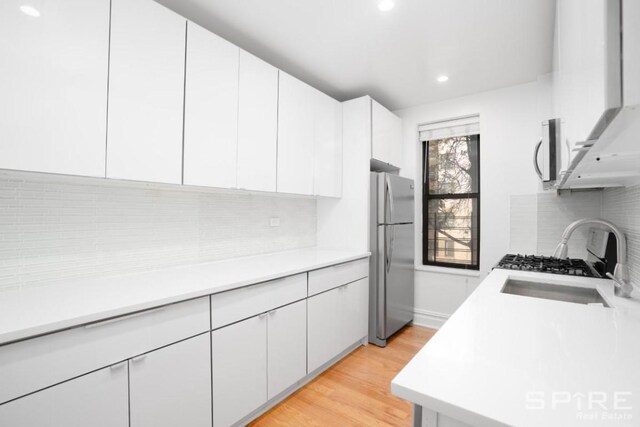 kitchen featuring light wood-type flooring, freestanding refrigerator, white cabinetry, wall chimney exhaust hood, and tasteful backsplash