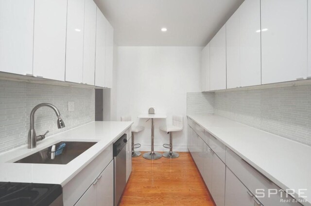 kitchen featuring a sink, dishwasher, white cabinets, and light wood finished floors