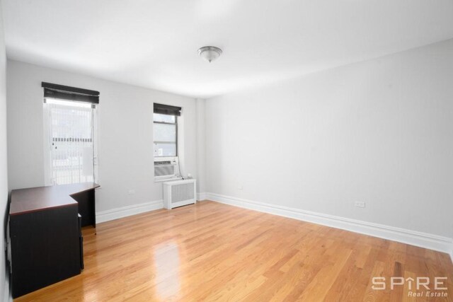 empty room featuring radiator heating unit, baseboards, and light wood finished floors