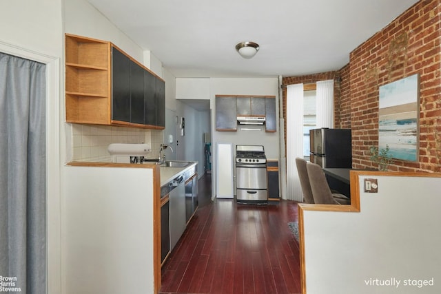 kitchen with dark wood-type flooring, sink, tasteful backsplash, appliances with stainless steel finishes, and brick wall