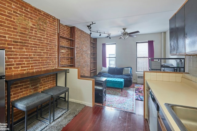 interior space with appliances with stainless steel finishes, rail lighting, brick wall, sink, and dark hardwood / wood-style floors