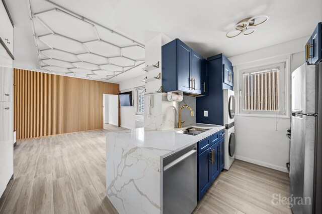 kitchen featuring stacked washer and dryer, appliances with stainless steel finishes, blue cabinets, light wood-style floors, and a sink