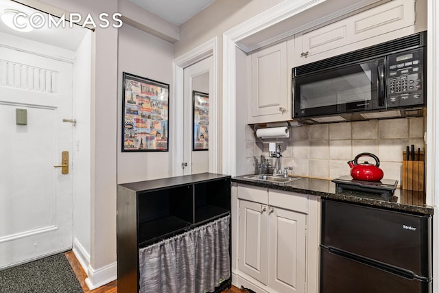 kitchen with a sink, white cabinetry, dark stone counters, black appliances, and tasteful backsplash