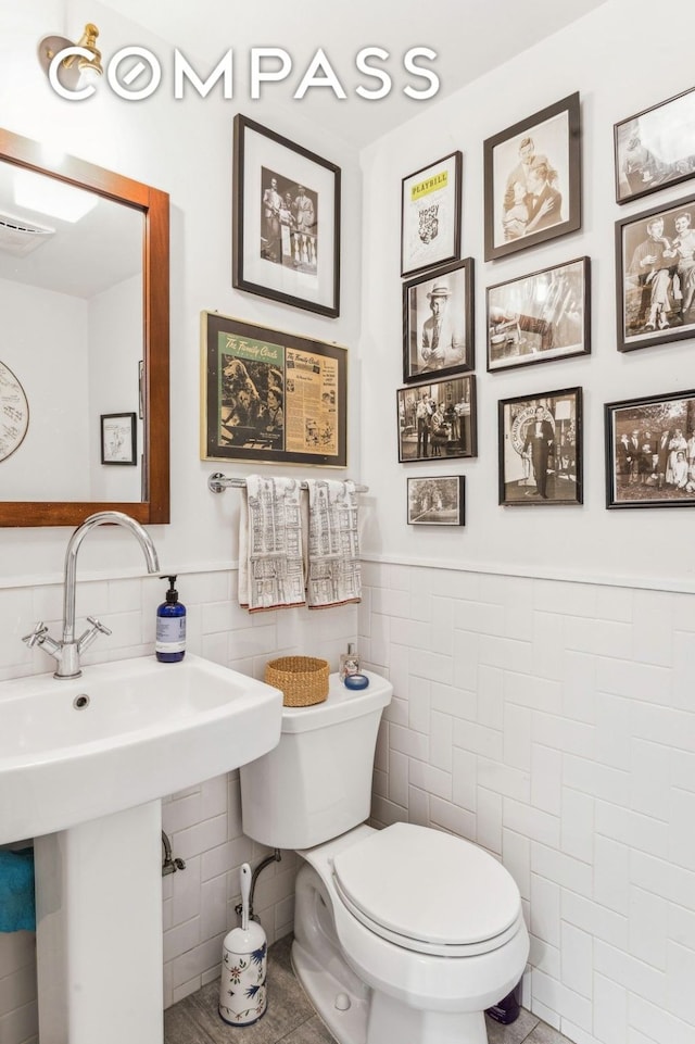 bathroom with tile walls, visible vents, toilet, wainscoting, and tile patterned flooring