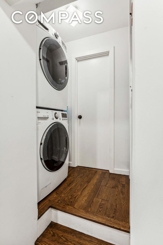 clothes washing area featuring stacked washing maching and dryer and wood finished floors