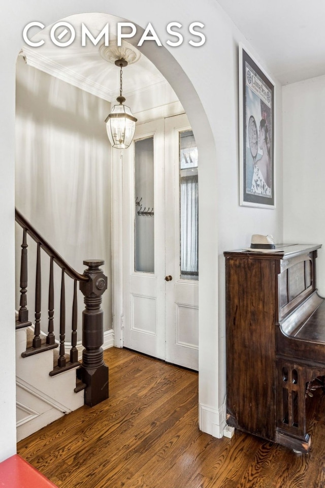 foyer entrance with arched walkways, a notable chandelier, baseboards, stairs, and dark wood finished floors