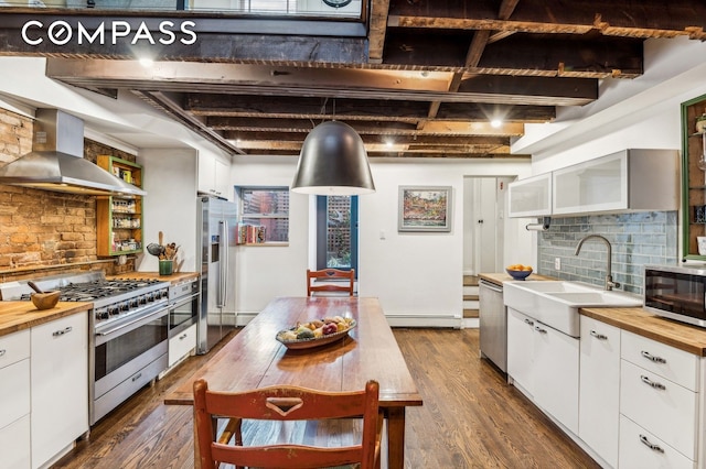 kitchen with appliances with stainless steel finishes, white cabinetry, a sink, and wall chimney range hood