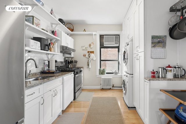 kitchen with radiator, stacked washing maching and dryer, open shelves, a sink, and appliances with stainless steel finishes