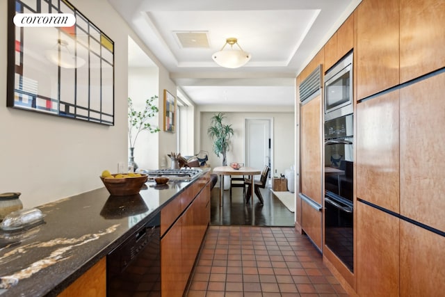 kitchen featuring a tray ceiling, black appliances, dark tile patterned floors, and dark stone countertops