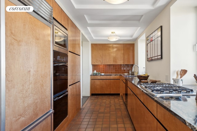 kitchen featuring backsplash, dark tile patterned flooring, sink, a tray ceiling, and built in appliances