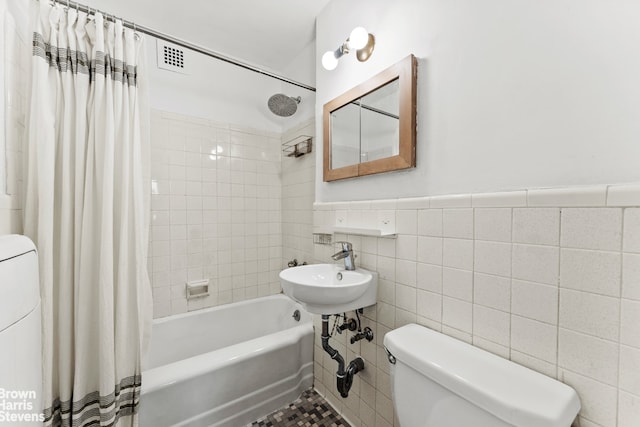 bathroom with tile walls, toilet, and shower / tub combo with curtain