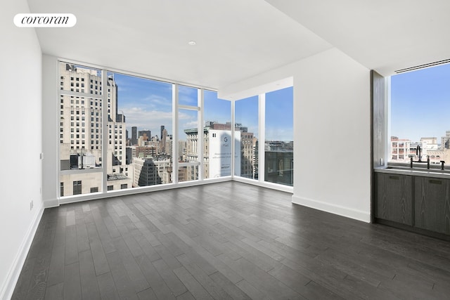 spare room with visible vents, baseboards, dark wood finished floors, expansive windows, and a view of city