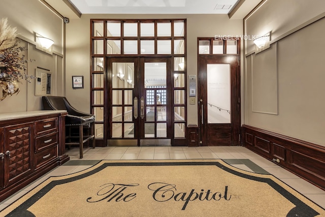 foyer featuring a decorative wall, light tile patterned floors, french doors, and wainscoting