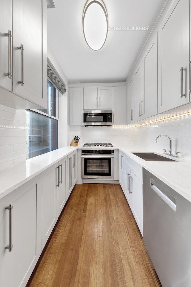 kitchen featuring light wood-style flooring, a sink, light countertops, appliances with stainless steel finishes, and tasteful backsplash