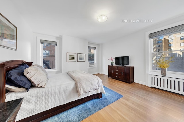 bedroom featuring multiple windows, radiator, and wood finished floors