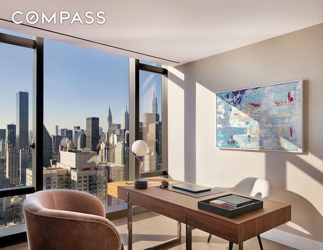 office area featuring a view of city, baseboards, floor to ceiling windows, and wood finished floors
