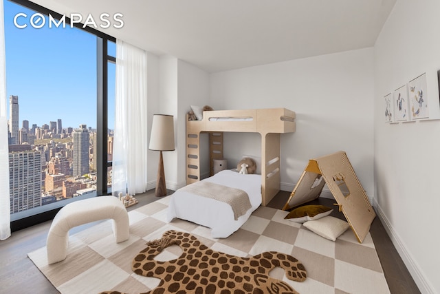 bedroom with a city view, floor to ceiling windows, baseboards, and wood finished floors