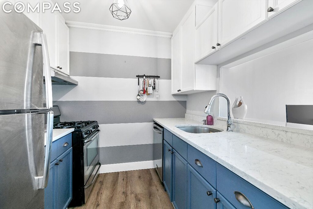 kitchen with appliances with stainless steel finishes, sink, white cabinets, light stone countertops, and blue cabinets