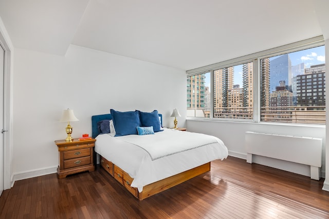 bedroom featuring a view of city, dark wood-style floors, and baseboards