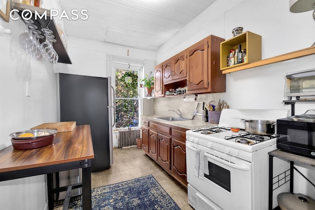 kitchen with open shelves, gas range gas stove, radiator heating unit, freestanding refrigerator, and a sink