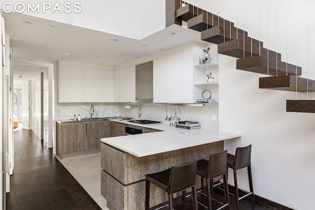 kitchen with white cabinetry, kitchen peninsula, decorative backsplash, stainless steel gas cooktop, and sink