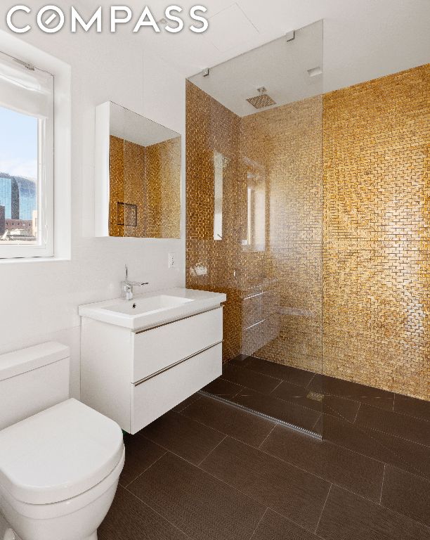 bathroom featuring tile patterned flooring, toilet, walk in shower, and vanity