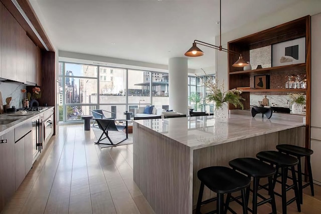 kitchen with decorative backsplash, modern cabinets, a breakfast bar area, light stone counters, and a peninsula