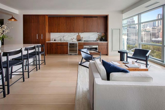 living area with wet bar, beverage cooler, a healthy amount of sunlight, and light wood finished floors