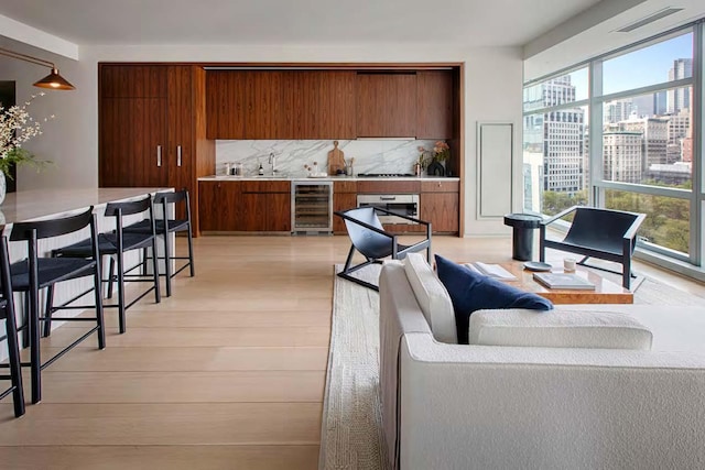living room with beverage cooler, plenty of natural light, light wood-style floors, and a view of city
