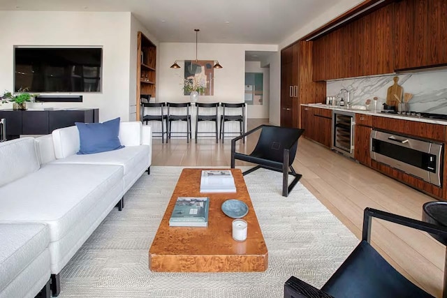 living area with light wood finished floors, beverage cooler, and wet bar