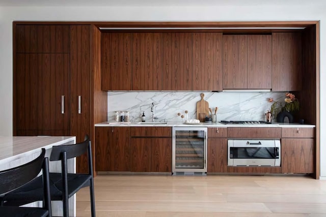 indoor wet bar featuring wine cooler, appliances with stainless steel finishes, backsplash, and light wood-style floors