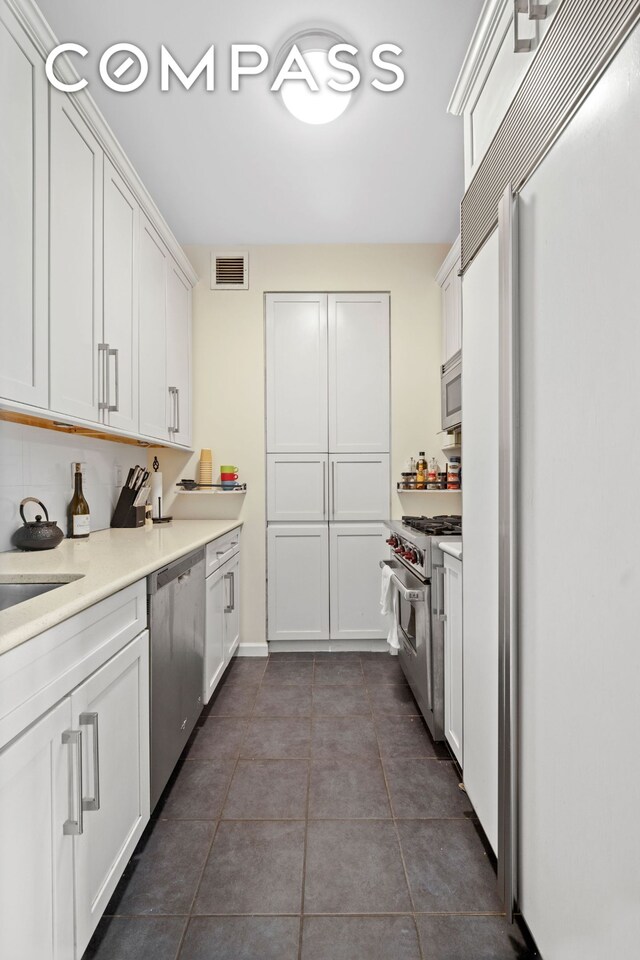 kitchen with high quality appliances, dark tile patterned floors, and white cabinets