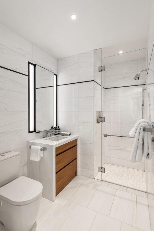 bathroom featuring vanity, toilet, tile walls, and walk in shower