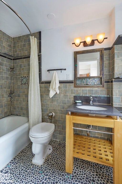 full bathroom featuring toilet, tile patterned flooring, tile walls, shower / bath combination with curtain, and sink