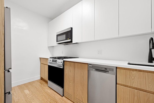 kitchen featuring appliances with stainless steel finishes, a sink, light wood-style floors, modern cabinets, and light countertops
