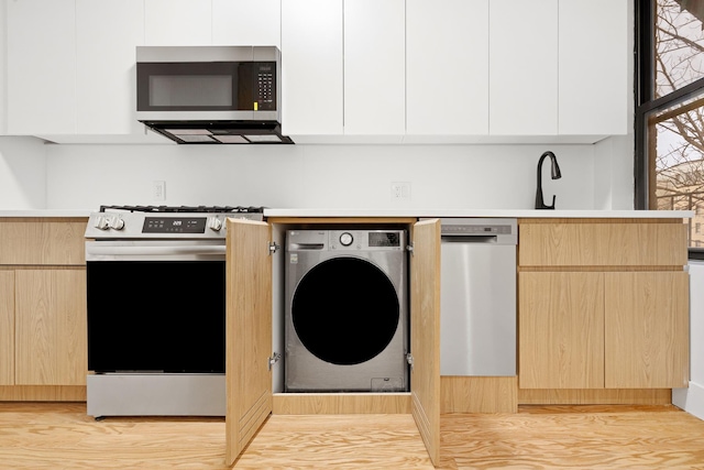 kitchen with light countertops, light brown cabinetry, appliances with stainless steel finishes, modern cabinets, and washer / dryer