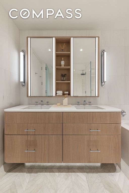 full bath with double vanity, a sink, and tile walls