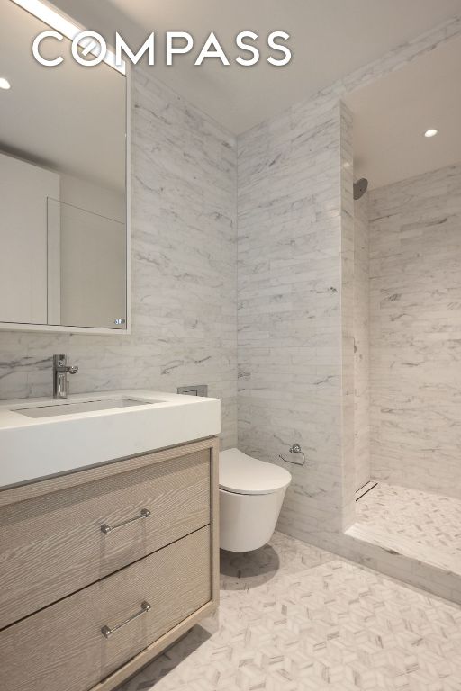 bathroom featuring toilet, vanity, a shower stall, and tile walls