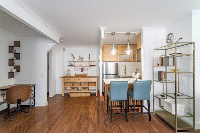 kitchen featuring a breakfast bar, stainless steel refrigerator, decorative light fixtures, ornamental molding, and dark wood-type flooring