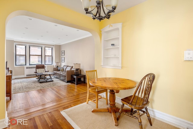 dining space with arched walkways, a chandelier, wood finished floors, crown molding, and baseboards