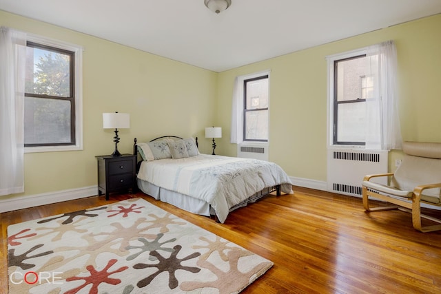 bedroom featuring radiator heating unit, wood finished floors, multiple windows, and baseboards