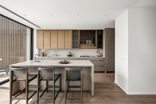 kitchen with light countertops, a sink, wood finished floors, a kitchen breakfast bar, and black electric cooktop