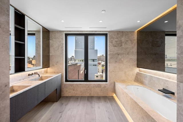 full bathroom featuring a garden tub, tile walls, recessed lighting, vanity, and wood finished floors