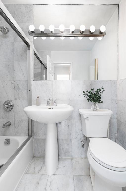 bathroom with toilet, bath / shower combo with glass door, and tile walls